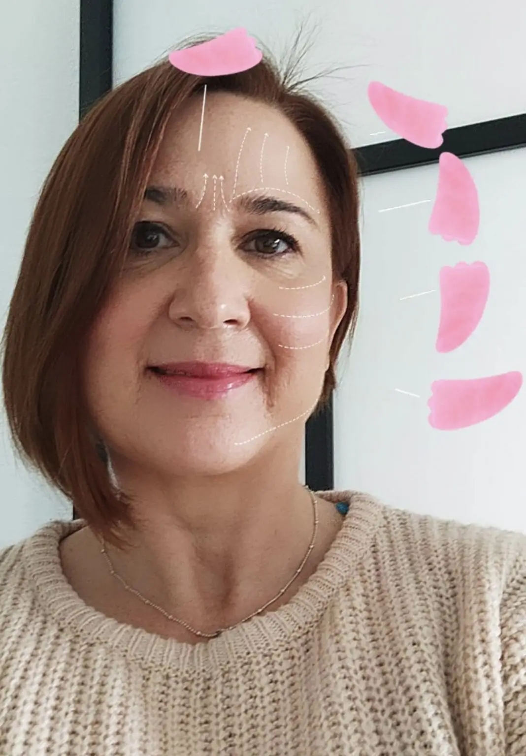 Valerie Millet Una mujer de pelo corto y castaño sonríe a la cámara. La imagen ha agregado formas rosadas y líneas blancas en su rostro que indican áreas específicas, posiblemente con fines cosméticos o de cuidado de la piel. Bienestar Holistico