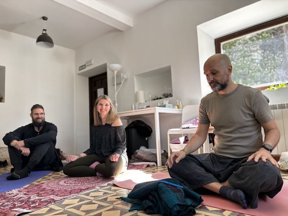 Valerie Millet Tres personas están sentadas con las piernas cruzadas sobre esteras de yoga en una habitación bien iluminada, participando en una sesión de meditación que promete empoderamiento. Bienestar Holistico