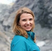 Valerie Millet Una mujer de cabello rubio con una chaqueta azul sonríe a la cámara con un terreno rocoso al fondo. Bienestar Holistico