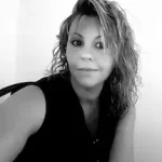 Valerie Millet Una fotografía en blanco y negro de una persona con cabello ondulado hasta los hombros, vestida con una blusa sin mangas y mirando directamente a la cámara. Bienestar Holistico